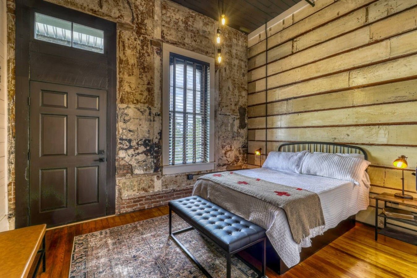 A bedroom with a large bed, a bench, a window, and a door.