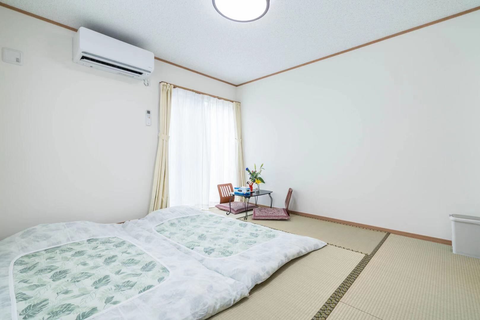 Une pièce avec un lit, une petite table et des chaises, et une fenêtre avec des rideaux.