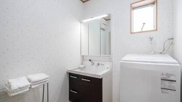 A small bathroom with a white sink, dark cabinet, and a mirror above it. There is a towel rack with towels and a small window with a wooden frame.