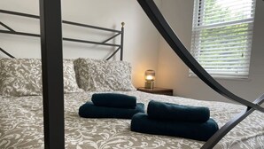 Un dormitorio con cama, almohadas y mesita de noche con lámpara.