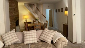 Una sala de estar con sofá, chimenea, mesa de comedor con sillas y una escalera que lleva a otra habitación.