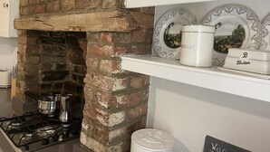 Una cocina con chimenea de ladrillo, estufa a gas y repisa con platos decorativos y un recipiente para mantequilla.