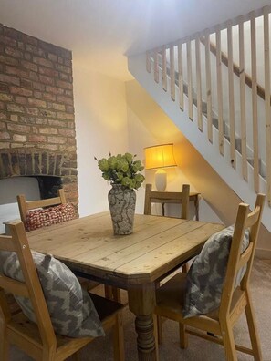 Un coin repas avec une table et des chaises en bois, un vase avec des plantes vertes, un mur en briques et un escalier avec une rampe.