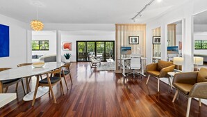 A spacious living area with a wooden dining table, comfortable seating, and a large window offering a view of greenery. - Fort Lauderdale~Saltwater Pool~Near Beach~Spacious (Fort Lauderdale)