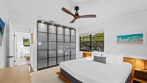 A modern bedroom with a large bed, a wooden nightstand, a ceiling fan, and a view of greenery through a window. - Fort Lauderdale~Saltwater Pool~Near Beach~Spacious (Fort Lauderdale)