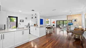 A modern kitchen with white cabinetry and a wooden floor, a dining area with a table and chairs, and a living space with a sofa and a TV. - Fort Lauderdale~Saltwater Pool~Near Beach~Spacious (Fort Lauderdale)