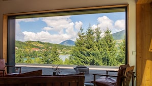 A room with a large window offering a view of a lake and mountains. There is a wooden bench and a table with a vase. - Veranda 4M  property (Colibita)