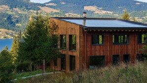 A modern wooden house with large windows and a solar panel roof, surrounded by forest and mountains. - Veranda 4M  property (Colibita)