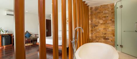 Un baño moderno con una bañera independiente grande, pilares de madera y una pared de ladrillo.