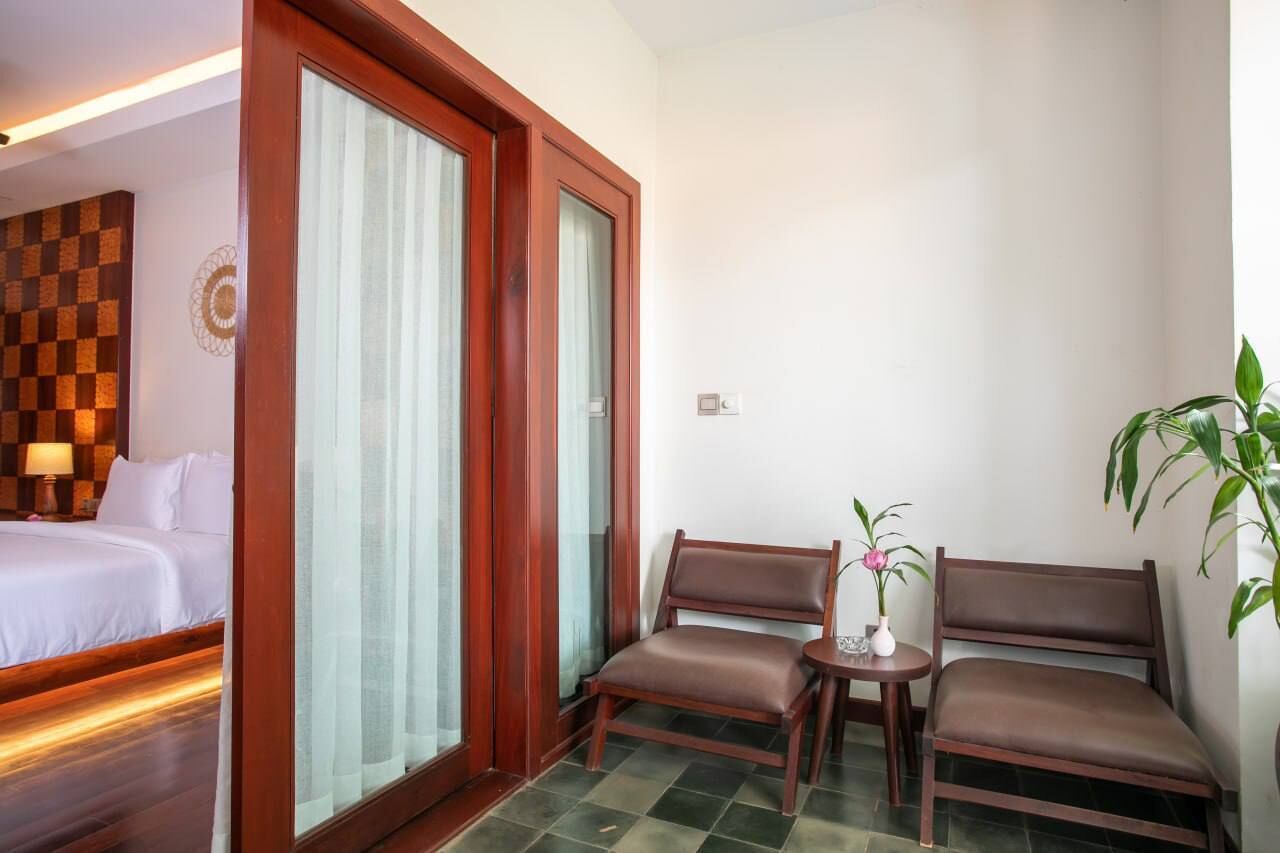 Habitación de hotel con una cama, una zona de estar con dos sillones, una mesita con un florero y una planta en maceta.