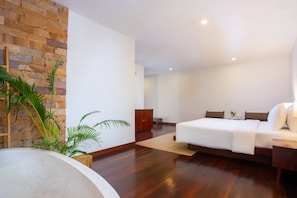 A modern hotel room with a wooden floor, a bed, a nightstand, a small cabinet, and a large potted plant. - Mera Residence (Siem Reap)