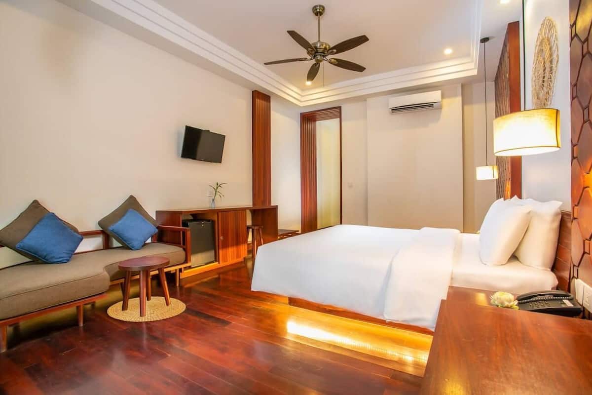 Habitación de hotel con cama, sofá, mesita, ventilador de techo, televisión y lámpara.