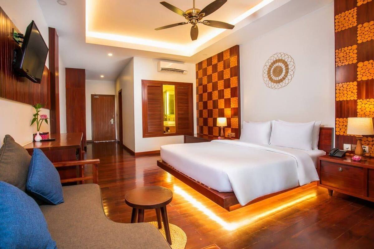 Una habitación de hotel con una cama grande, un ventilador de techo, un televisor montado en la pared, suelo de madera y un diseño de pared a cuadros.