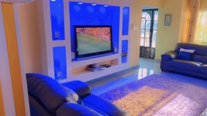Ein Wohnzimmer mit Flachbildfernseher an der Wand, einer Couch und einem gemusterten Teppich.