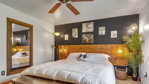 Un dormitorio con cabecera de madera, un espejo grande y obras de arte en la pared.