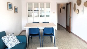 Ein Essbereich mit Holztisch und blauen Stühlen, eine blaustürkisene Couch mit einem gemusterten Kissen sowie ein Flur mit einer Tür und Hüten an der Wand.