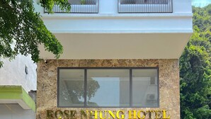 The Rose Hung Hotel entrance with a stone facade, large glass windows, and outdoor seating area with potted plants. - Rose Nhung Hotel Catba (Hai Phong)