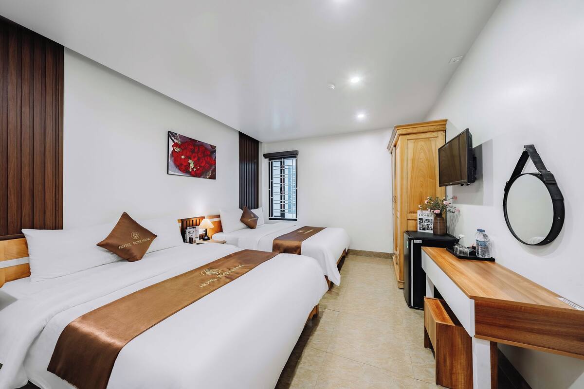 Une chambre d’hôtel avec deux lits, un bureau en bois, une télévision et une fenêtre avec des barreaux.