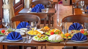 A restaurant with wooden tables and chairs, each set with blue napkins, plates of food, and glasses of water. - Rose Nhung Hotel Catba (Hai Phong)