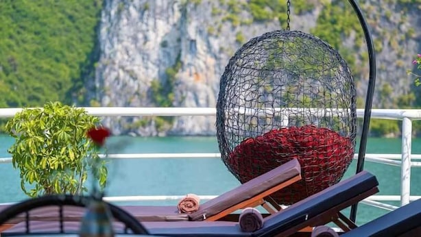 A sun lounger with a netted hanging chair and a potted plant on a balcony with a view of cliffs and water. - Rose Nhung Hotel Catba (Hai Phong)
