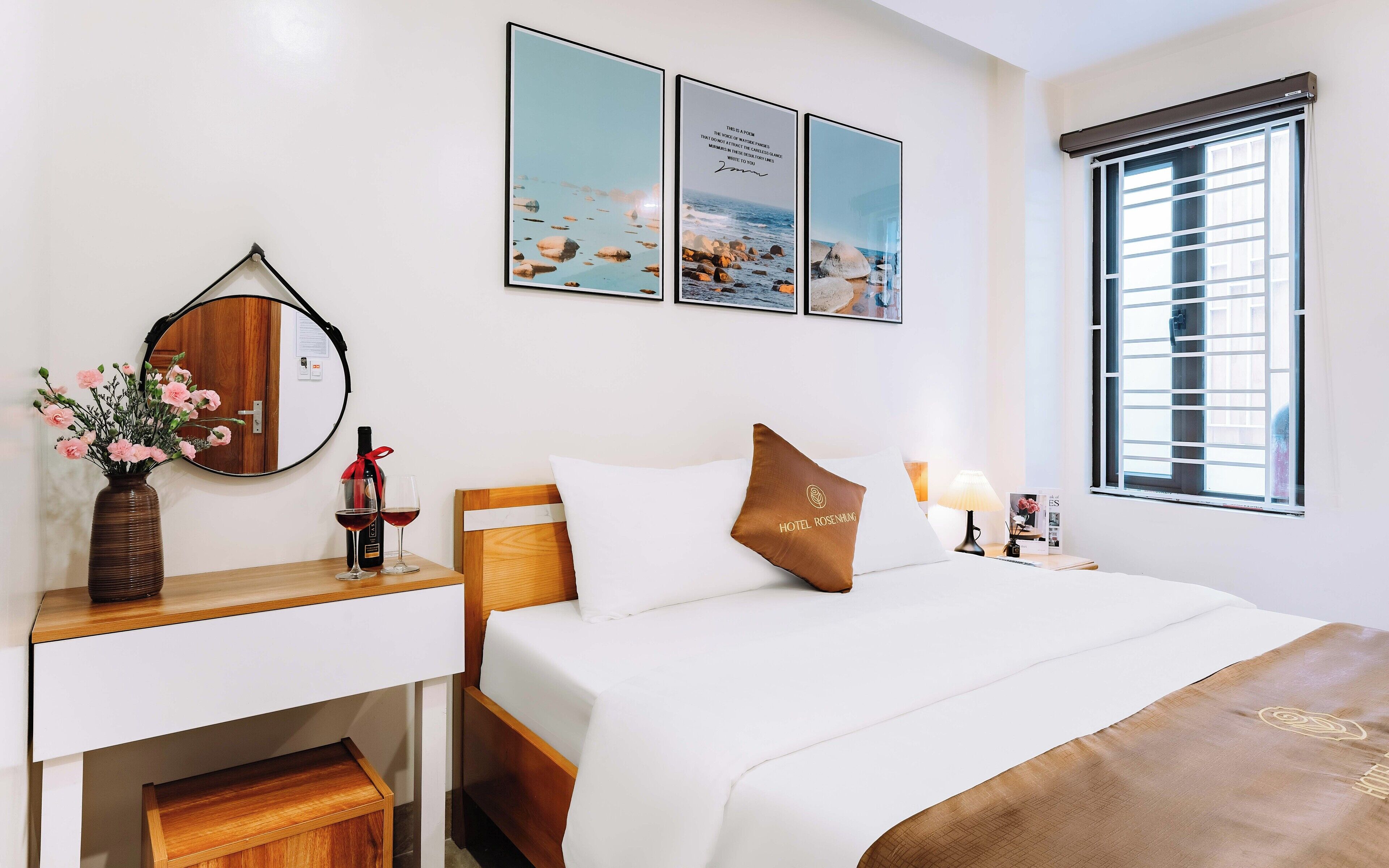 A hotel room with a bed, bedside table, lamp, and a window with blinds.