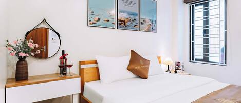 A hotel room with a bed, bedside table, lamp, and a window with blinds.