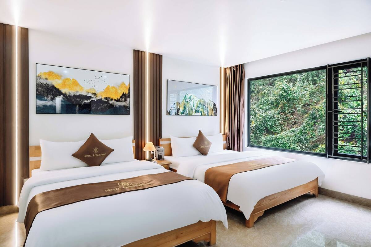 Une chambre d’hôtel avec deux lits, une grande fenêtre donnant sur un paysage verdoyant et des œuvres d’art accrochées aux murs.
