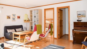 A living room with a sofa, a table, a chair, a bookshelf, a piano, and a bunk bed. - Cozy home in ålem with kitchen (Ålem)