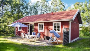 A red wooden cabin with a tiled roof, a patio with chairs and a table, and a covered outdoor seating area. - Cozy home in ålem with kitchen (Ålem)