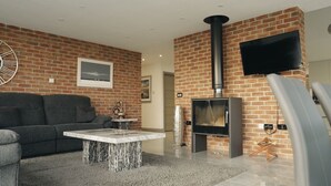 A living room with a brick wall, a fireplace, a sofa, a coffee table, and a TV mounted on the wall. - Hollywood vibes in pembrokeshire (Haverfordwest)