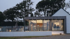 A modern house with a glass facade, a dining area, and a visible kitchen. - Hollywood vibes in pembrokeshire (Haverfordwest)