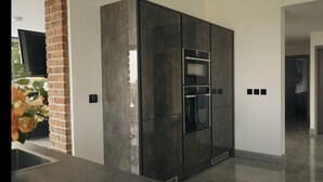 A modern kitchen with a built-in oven and microwave, a brick accent wall, and a clean, tiled floor. - Hollywood vibes in pembrokeshire (Haverfordwest)