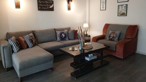 A modern living room with a grey sofa, a red armchair, and a coffee table. There are wall-mounted lights and framed pictures on the wall. - Apartment in Jounieh, sea view, 6th floor, wifi (Keserouan)