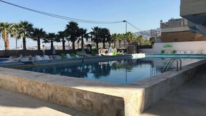 A rooftop pool with lounge chairs and palm trees, surrounded by a cityscape. - Apartment in Jounieh, sea view, 6th floor, wifi (Keserouan)