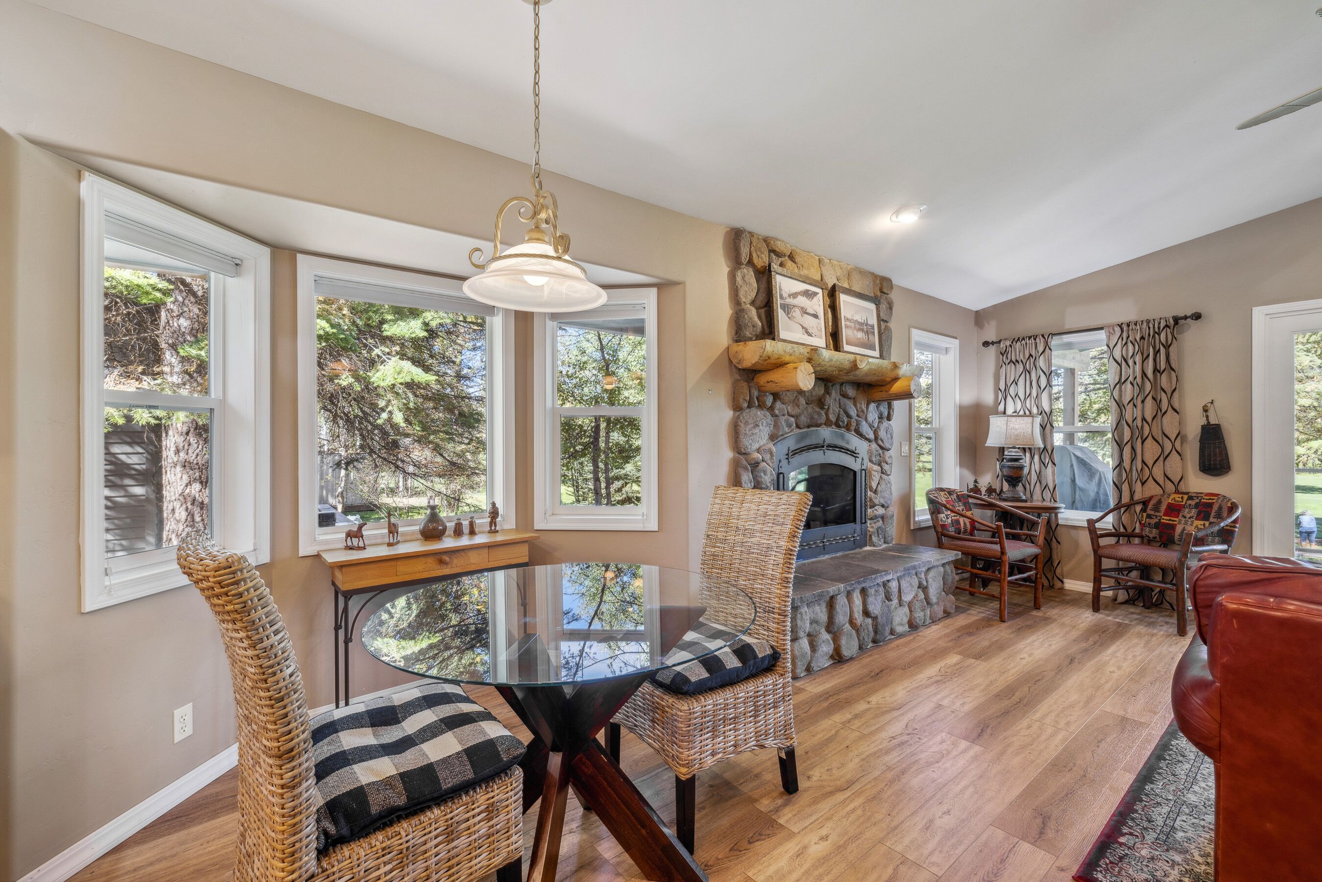 A spacious living area with a stone fireplace, large windows, and a dining table with wicker chairs.