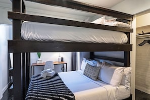 A bunk bed room with a bedside table, a lamp, and a hanging coat rack.