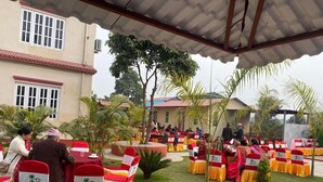 An outdoor event with rows of tables and chairs, some with red and yellow tablecloths, and a building in the background. - Hotel Kavya Inn Chitwan (Bharatpur)