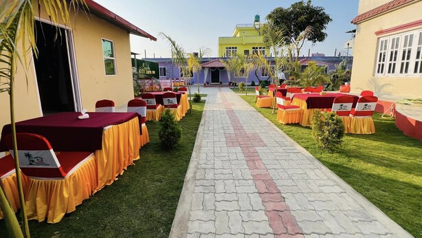 A hotel courtyard with rows of tables and chairs, a paved walkway, and a building in the background. - Hotel Kavya Inn Chitwan (Bharatpur)