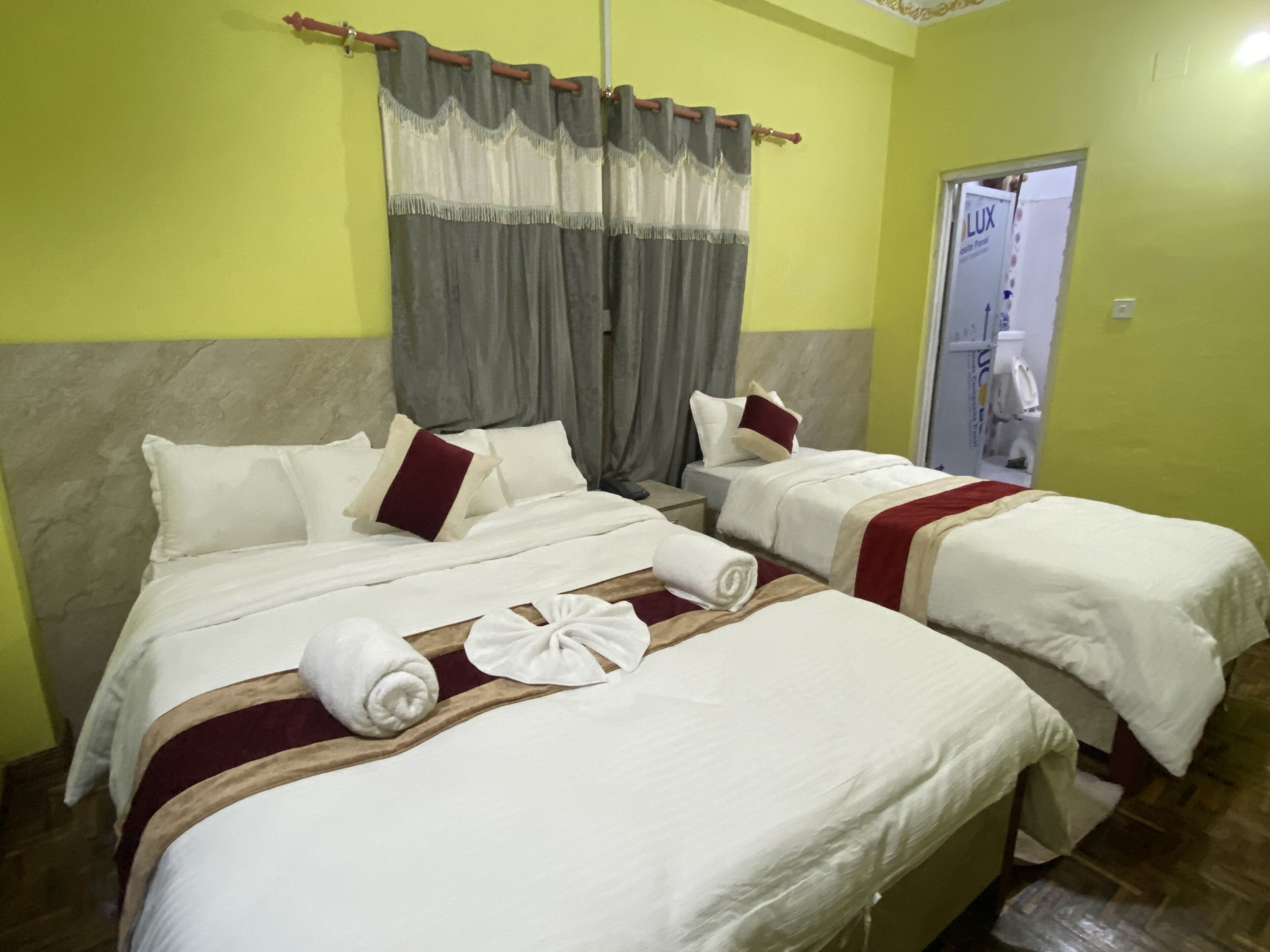 Een hotelkamer met twee bedden, elk voorzien van witte beddengoed en rode accenten, een houten hoofdbord en een grijze gordijn.