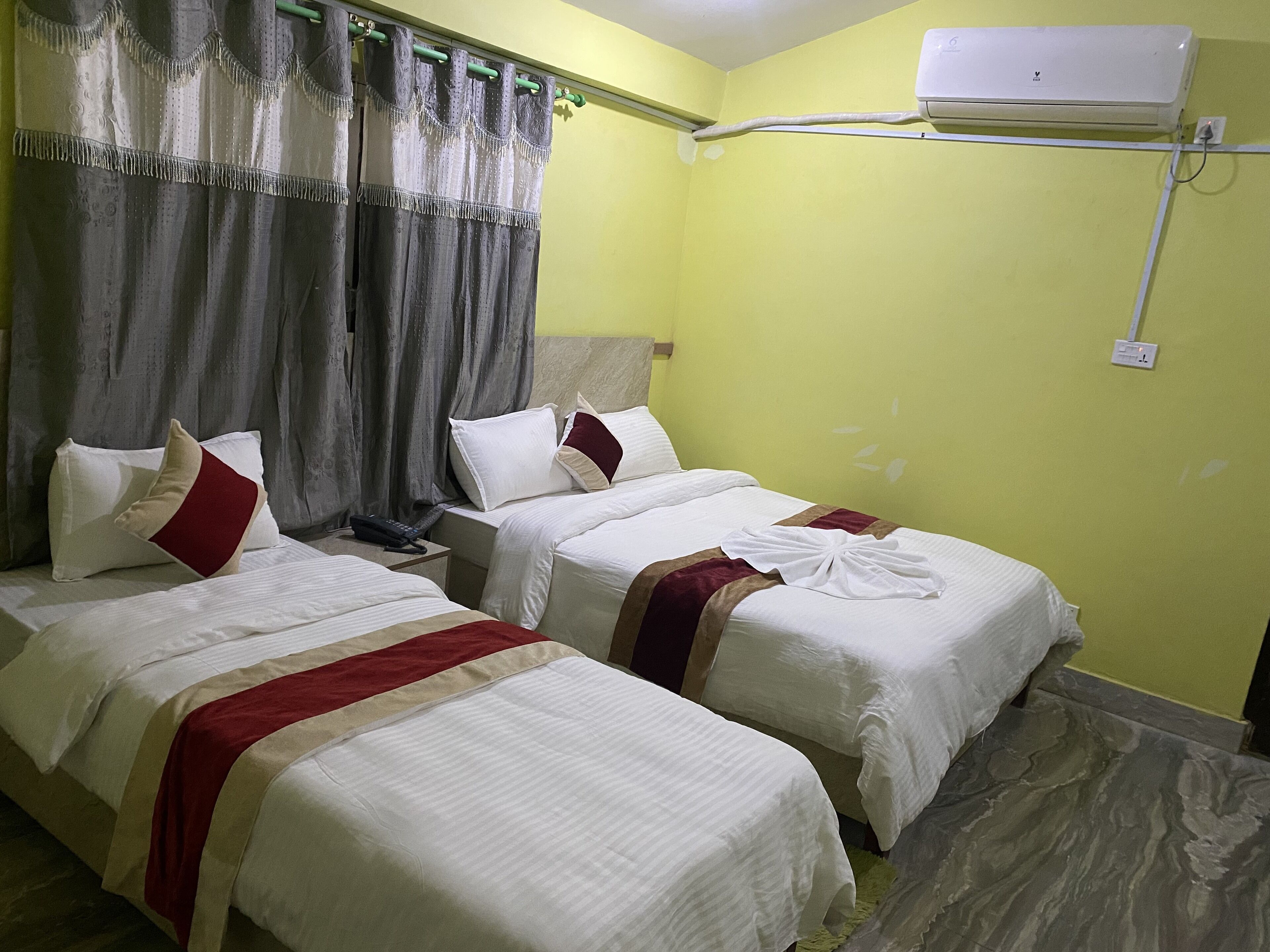 A hotel room with two beds, a telephone, and an air conditioning unit.