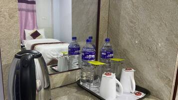 Habitación de hotel con cama, un descanso con botellas de agua, una tetera y un recipiente con tazas blancas.