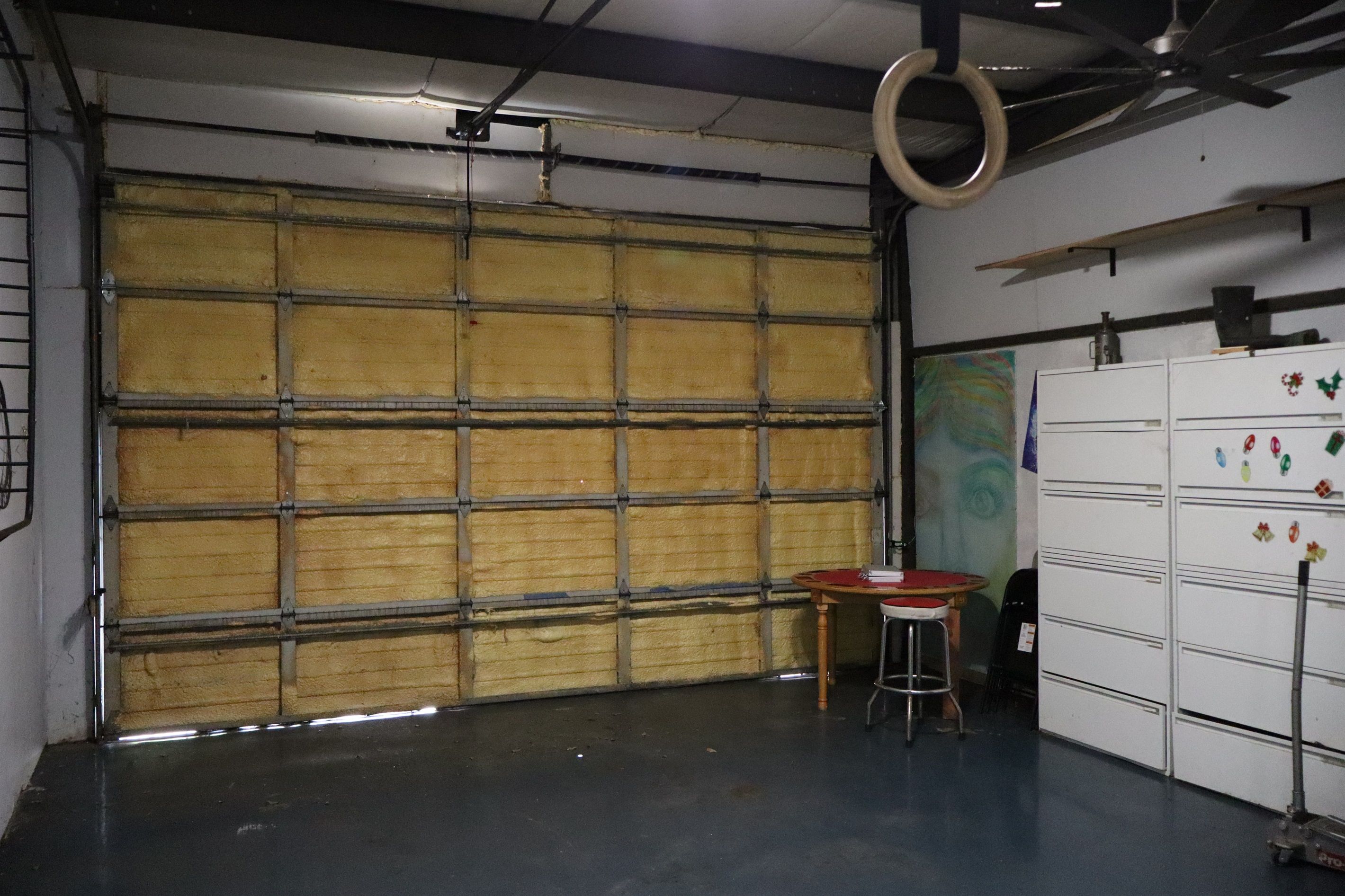 Eine Garage mit einer großen Metalttür, einem Tisch mit Stühlen und einem Kühlschrank mit Magneten.