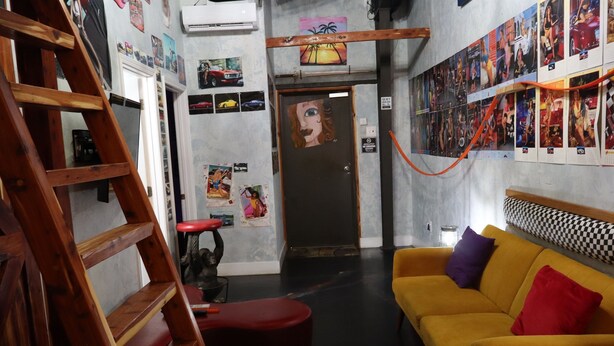 A room with a wooden ladder, a red stool, a yellow sofa with multiple cushions, and a door with a painting.