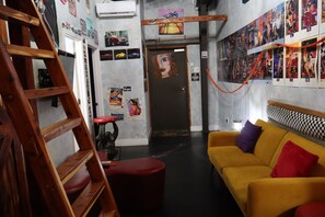 A room with a wooden ladder, a red stool, a yellow sofa with multiple cushions, and a door with a painting. - Downtown Chop Shop house, HUGE garage pets allowed (fort smith)