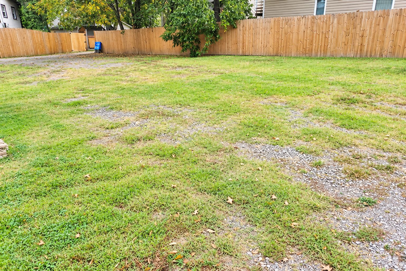 Un jardin avec une clôture en bois, un arbre et un chemin de gravier.