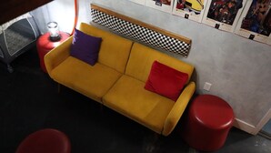 A yellow sofa with red and purple cushions, a red stool, and a small table with a candle.