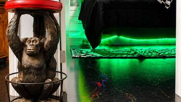 Une chambre avec un lit doté d’un éclairage vert sous le cadre, une sculpture de singe posée sur une table et un coussin à carreaux sur le lit.