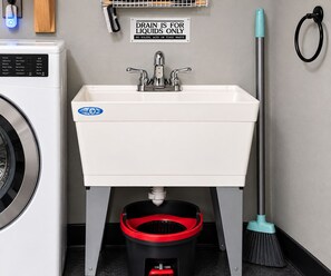 A laundry room with a sink, a sign indicating the drain is for liquids only, a mop, and a broom. - Downtown Chop Shop house, HUGE garage pets allowed (fort smith)