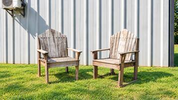 Two wooden Adirondack chairs with metal frames, positioned on a grassy lawn in front of a corrugated metal wall.