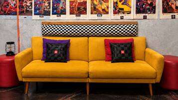 A yellow sofa with checkered cushions, a red stool, and a wall with calendars.